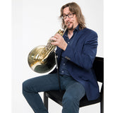 A man sitting on a chair, playing his horn with the ergo brass horn support system