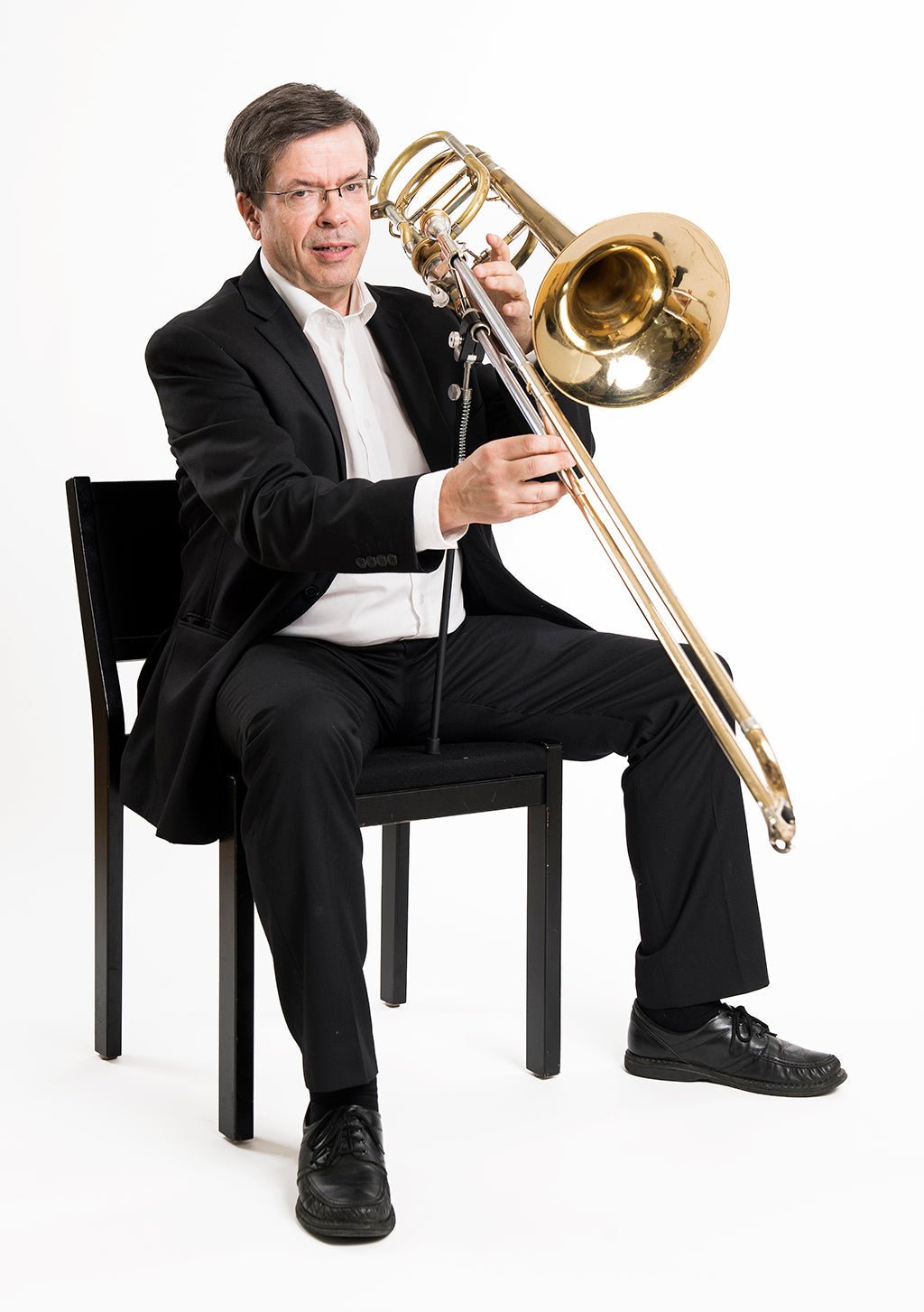 A man sitting on a chair using the ergobrass trombone support system to hold his trombone