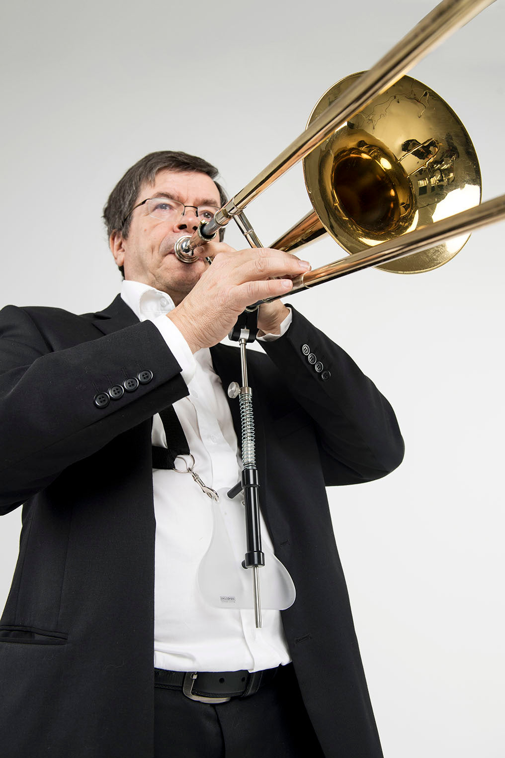 A standing man playing the trombone with the ergobrass trombone support system