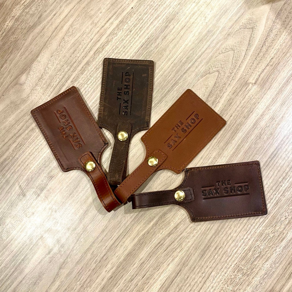 Four leather luggage tags that have "Sax Shop" imprinted on them. They are different colors.